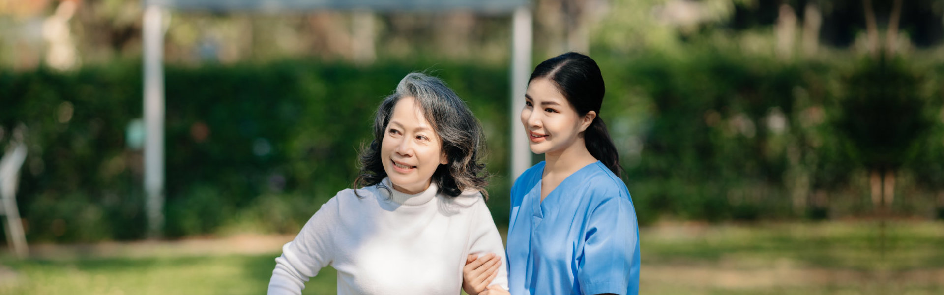 Asian young caregiver nurse support senior walking outdoors.